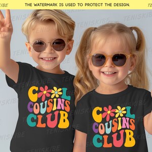 K&ouml;nnte beinhalten: Zwei Kinder tragen schwarze T-Shirts mit einem bunten "Cool Cousins Club"-Motiv. Die Kinder tragen Sonnenbrillen und l&auml;cheln.