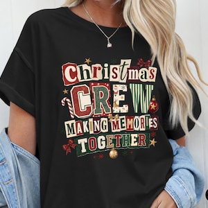 Peut inclure: Un t-shirt noir à manches courtes avec une impression graphique portant le texte Christmas CREW MAKING MEMORIES TOGETHER. Le motif inclut des éléments festifs comme un sucre d'orge, une boule rouge, une boule dorée, des étoiles et des nœuds.