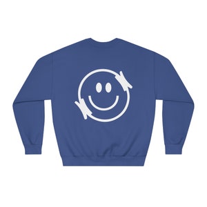 Könnte beinhalten: Ein königsblauer Pullover mit einem weißen Smiley-Motiv auf der Rückseite. Der Smiley hat einen weißen Umriss und zwei weiße Augen.
