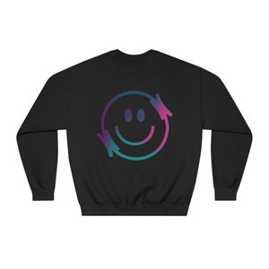 Könnte beinhalten: Schwarzer Pullover mit einem Smiley-Motiv in Blau- und Rosatönen mit Pfeilen auf beiden Seiten des Gesichts.