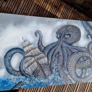 Op de afbeelding: Een rechthoekig canvas schilderij met een grote, donkerblauwe octopus met getextureerde zuignappen die zijn tentakels om een houten zeilschip wikkelt. De scène speelt zich af tegen een bewolkte, lichtgrijze lucht met woelige blauwe golven.
