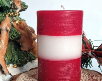 May include: A red and white striped pillar candle with a textured surface. The candle is sitting on a wooden slice.