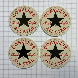 Può includere: Quattro toppe per scarpe Converse All Star bianche con cuciture rosse e una stella nera al centro. Il testo "Converse", "Chuck Taylor" e "All Star" è in rosso.