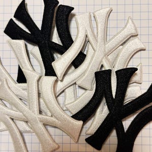 Puede incluir: Parches bordados con la forma de la letra "Y" en blanco y negro. Los parches están hechos de una tela texturizada y están dispersos sobre un fondo de cuadrícula. Ideales para ropa o proyectos de manualidades.