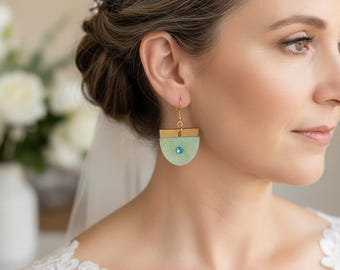 May include: A dangle earring featuring a gold-toned metal bar attached to a light green, semi-circular pendant. The pendant is accented with a small, round, bright blue crystal centered on its surface. The earring hangs from a gold-toned hook.