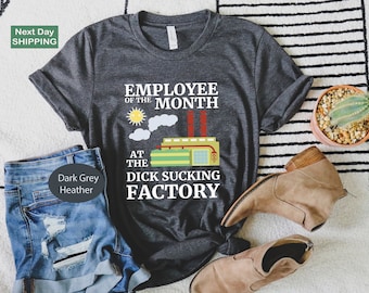 Puede incluir: Camiseta gris oscuro jaspeado con el texto "EMPLOYEE OF THE MONTH AT THE DICK SUCKING FACTORY". El gráfico incluye una ilustración de una fábrica, un sol y nubes. La camiseta se combina con pantalones cortos vaqueros y botas.
