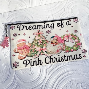 May include: A rectangular cosmetic bag with a black zipper and a pink Christmas theme. The bag features the text "Dreaming of a Pink Christmas" with illustrations of a gingerbread man, Santa Claus, and a Christmas tree.