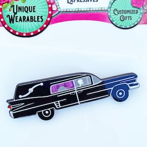 May include: Black hearse pin with white accents, featuring a skeleton passenger and purple curtains. The pin is a unique wearable item. The image also includes text that says "Unique Wearables", "Chroma Expressives", and "Customized Gifts".