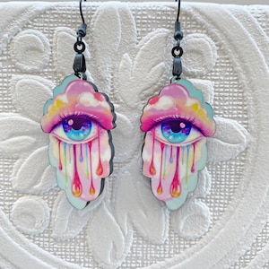 May include: A pair of dangle earrings with a pink and blue cloud design. Each cloud has a single eye with a blue iris and a rainbow of colors dripping from the eye.