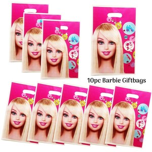 Op de afbeelding: Tien roze cadeauzakjes met een blond poppengezicht met blauwe ogen en roze lippen. De zakjes hebben een handvat aan de bovenkant en zijn versierd met kleurrijke cirkels met afbeeldingen van schoenen en andere accessoires. De tekst "10pc Barbie Giftbags" staat op de zakjes.