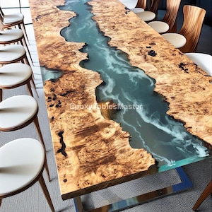 May include: A large, rectangular wooden table with a river-like design made of blue resin. The table's surface is a light brown with a unique wood grain pattern. The table is supported by a silver metal base. The text "EpoxyTablesMaster" is visible.