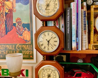 May include: A vertical wall-mounted weather station featuring three octagonal wooden frames. The top unit is a thermometer, the center is an analog clock with Roman numerals, and the bottom unit is a barometer. Each component has a silver bezel.