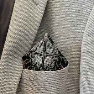 Op de afbeelding: Close-up van een lichtgrijze blazer met een zwart-wit patroon pochet. De pochet heeft een geometrisch ontwerp. De stof van de blazer heeft een subtiele textuur en de pochet voegt een contrasterend element toe.