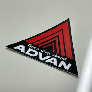 May include: A black and red triangle sticker with the word "ADVAN" in white letters and the text "Get a step ahead" in white letters.