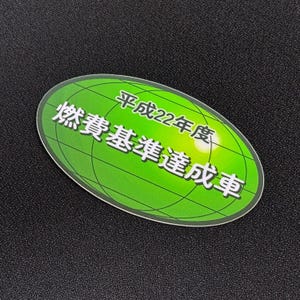 May include: An oval-shaped green sticker with Japanese text and a grid pattern. The text is in white and includes the characters for "Heisei 22", "fuel consumption standards", and "achieved vehicle". The sticker has a white border.