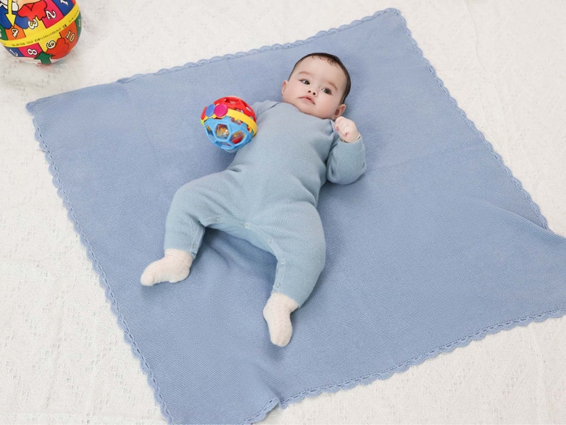 Baby in blauem Merino-Strampler liegt auf Babydecke