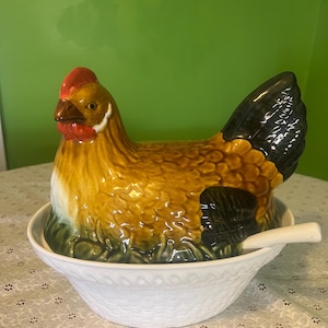 May include: A ceramic hen-shaped serving dish with a white bowl base and a matching spoon. The hen is brown, yellow, and black with a red comb. The bowl has a woven pattern.