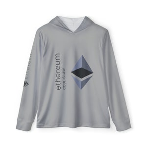 May include: A light grey hoodie with long sleeves. The shirt displays the Ethereum logo and the text "Ethereum CODE IS LAW" in black. The Ethereum logo is a stylized, geometric shape in shades of blue and grey.