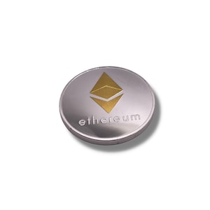 May include: A silver-coloured coin with a gold Ethereum logo and the word "ethereum" printed on it.