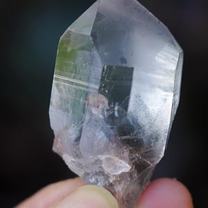 Puede incluir: Un cristal de cuarzo transparente con doble terminaci&oacute;n, tambi&eacute;n conocido como cristal de doble punta. El cristal tiene una apariencia natural y en bruto con inclusiones y estr&iacute;as visibles.