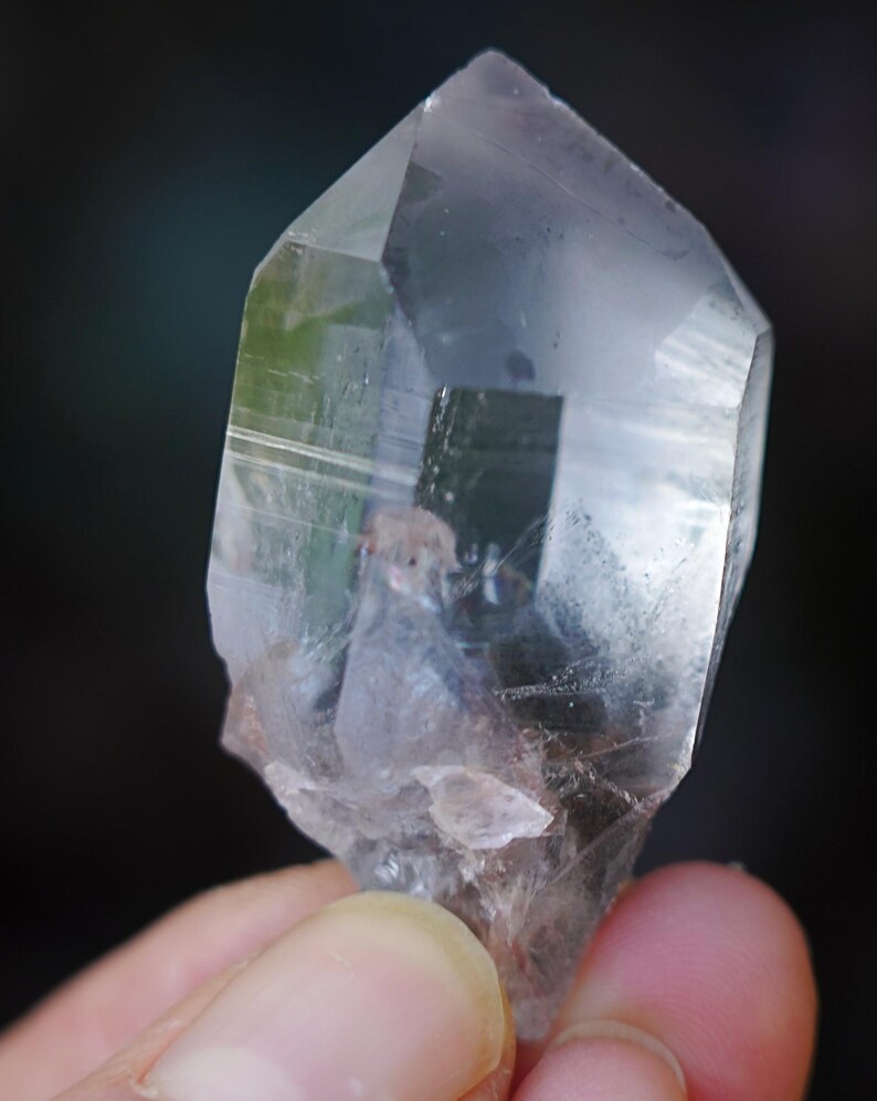 Puede incluir: Un cristal de cuarzo transparente con doble terminaci&oacute;n, tambi&eacute;n conocido como cristal de doble punta. El cristal tiene una apariencia natural y en bruto con inclusiones y estr&iacute;as visibles.