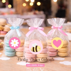 Pode incluir: Três sacos de celofane cheios de macarons coloridos, amarrados com fitas. Cada saco apresenta um adesivo diferente: uma margarida branca, uma abelha amarela e um coração rosa. O texto "Party Decor Cutouts" é visível.