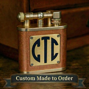 May include: A rectangular metal lighter with a brushed brass top mechanism and a textured copper-toned body. A square brass plate is centered on the front, featuring the black engraved letters CTC. A banner at the bottom reads Custom Made to Order.