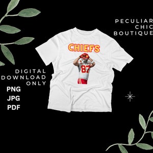 Puede incluir: Camiseta blanca con la palabra "CHIEFS" en letras naranjas y un jugador de fútbol americano que lleva una camiseta roja y amarilla con el número 87 en la parte delantera.