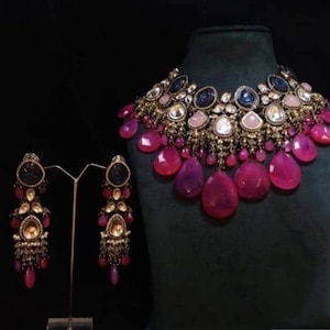 Peut inclure: Un ensemble collier et boucles d'oreilles luxueux. Le collier présente une base en métal doré ornée de pierres précieuses roses, violettes et bleues. Les boucles d'oreilles reprennent le design du collier, avec une palette de couleurs similaire et des pierres en forme de goutte.