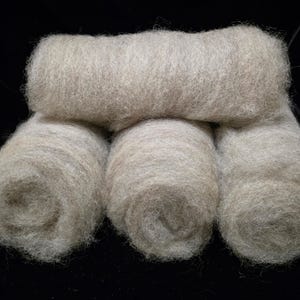 May include: Four rolls of light beige, unspun wool fiber arranged in a stack. The texture of the wool is soft, airy, and fibrous, with a natural, slightly variegated appearance in shades of cream and tan, showcasing the raw, fluffy material.