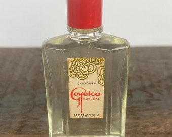 May include: A small, clear glass bottle of cologne with a red plastic cap. The label reads "Colonia Goyesca Natural Myrurgia Españ", with a floral design.