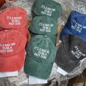 May include: A collection of six baseball caps in various colors, each featuring the embroidered text "It's a bad day to be a hot dog".