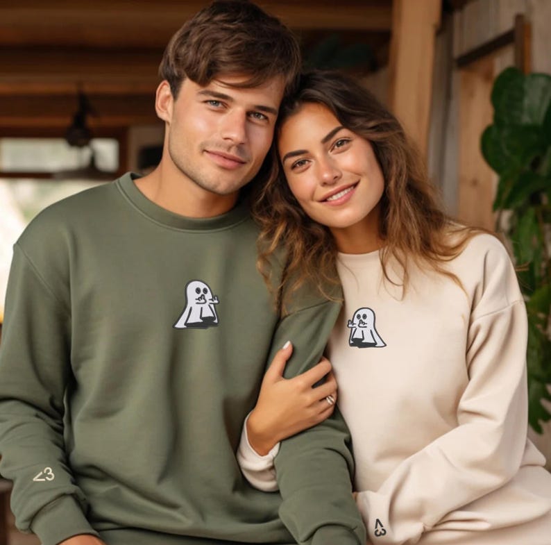 Pu&ograve; includere: Una felpa girocollo verde oliva e una felpa girocollo beige, entrambe caratterizzate da un piccolo ricamo sul petto raffigurante un fantasma bianco che fa un gesto con la mano e un piccolo simbolo "<3" ricamato sul polsino della manica.