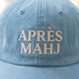 May include: Light blue baseball cap with the embroidered text "APR&Egrave;S MAHJ" in white. The cap has a curved brim and a classic six-panel design. A casual accessory for everyday wear.