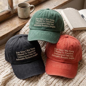 May include: Three baseball caps in green, black, and terracotta, each featuring the embroidered text: Ever Since I Was Young I Wanted To Transform Unstructured Data Into Actionable Business Insights. The caps have a structured crown and curved brim.