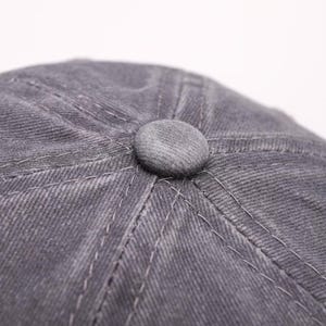 May include: Close-up of a gray newsboy cap with a rounded top and a small, matching button at the center. The cap features visible stitching and a textured fabric, suggesting a durable material.