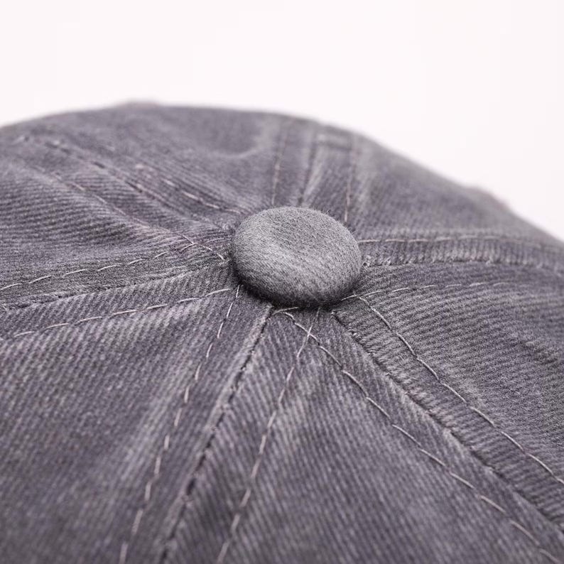 May include: Close-up of a gray newsboy cap with a rounded top and a small, matching button at the center. The cap features visible stitching and a textured fabric, suggesting a durable material.