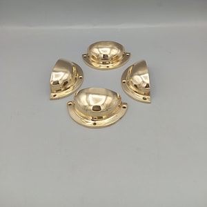 May include: Four gold-toned metal cabinet door pulls with a rounded, slightly curved shape. The pulls have a smooth, polished finish.