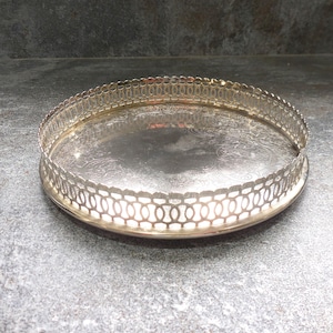 Peut inclure: Un plateau rond en métal argenté présentant un motif floral en relief complexe sur la base et un bord ajouré surélevé avec un design répétitif de découpes ovales. La surface présente une finition polie et réfléchissante sur toute la pièce.