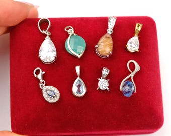 May include: A collection of gemstone pendants in various shapes and colors, including clear, blue, green, and brown. The pendants are displayed on a red velvet surface. Some have silver or gold settings.
