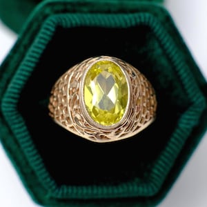 Può includere: Un anello d'oro con una gemma gialla ovale. L'anello presenta un intricato design traforato attorno alla gemma. L'anello è presentato in un cofanetto di velluto verde scuro.