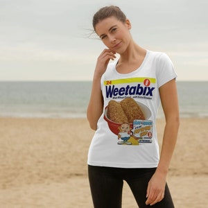 May include: A white t-shirt with a vintage Weetabix cereal box graphic. The box features a cartoon character holding two Weetabix biscuits. The text on the box reads "Weetabix Whole Wheat Cereal with Extra Vitamins".