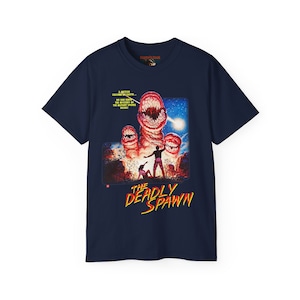 Puede incluir: Una camiseta azul marino con un estampado gráfico de un cartel de película para "The Deadly Spawn". El cartel presenta una gran criatura roja de múltiples bocas con un hombre y una mujer huyendo de ella. El texto en el cartel dice "Un meteorito se estrelló contra la tierra... ¡Nadie sabía la historia de los deportes mutantes en el interior!"
