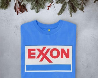 Könnte beinhalten: Ein hellblaues T-Shirt mit Rundhalsausschnitt und einem rechteckigen Aufdruck auf der Brust. Der Aufdruck zeigt den roten Schriftzug EXXON auf weißem Grund, platziert über einem durchgehenden blauen horizontalen Streifen im weißen Rahmen.