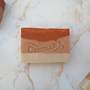 May include: A three-layered bar of soap with a brown, pink, and white colour scheme. The soap has the words "Camille's" embossed on the pink layer.