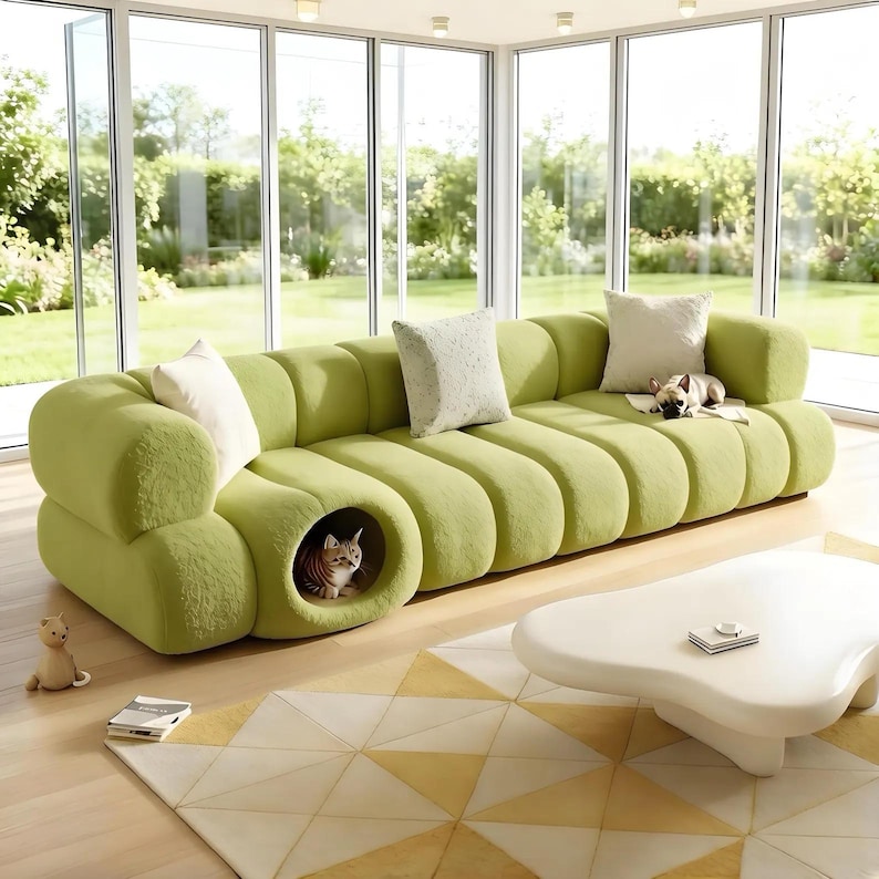 May include: A lime green sofa with a unique, rounded design. The sofa features a built-in cat bed and is adorned with several decorative pillows. A small dog rests on the sofa, and a cat is inside the cat bed. A white coffee table and a geometric rug are in front of the sofa.