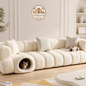 May include: Cream-colored, modern sofa with a built-in cat bed. The sofa has a rounded, textured design and includes decorative pillows. A small dog rests on the sofa. The logo "LittleHavenCooo" is visible on the wall.