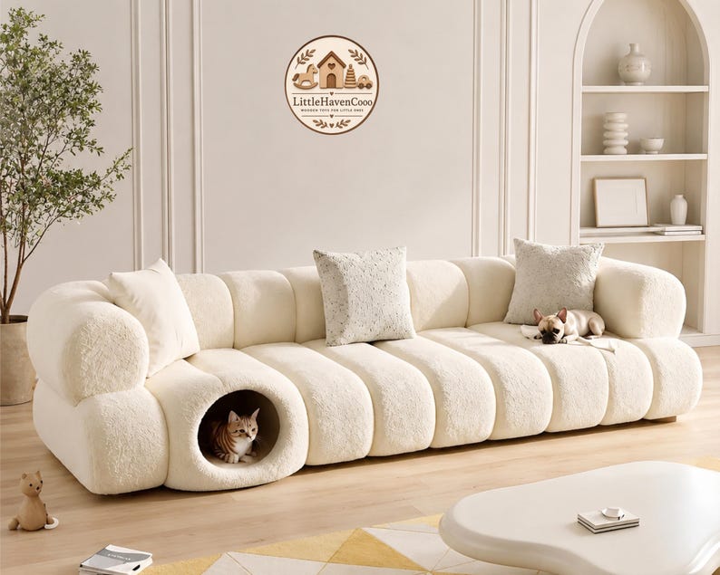 May include: Cream-colored, modern sofa with a built-in cat bed. The sofa has a rounded, textured design and includes decorative pillows. A small dog rests on the sofa. The logo "LittleHavenCooo" is visible on the wall.