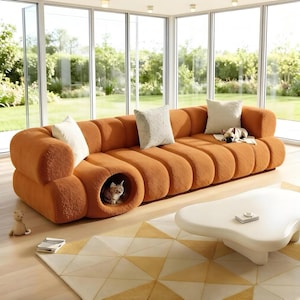 May include: An orange, modular sofa with a unique design, featuring rounded sections and a built-in cat bed. The sofa is adorned with several decorative pillows and a small dog toy. A white, organic-shaped coffee table sits in front of the sofa.