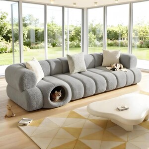May include: A large, gray, modern sofa with a built-in cat bed. The sofa has a rounded design and is adorned with several throw pillows. A cat is inside the cat bed. A small dog rests on the sofa. The sofa sits on a patterned rug.